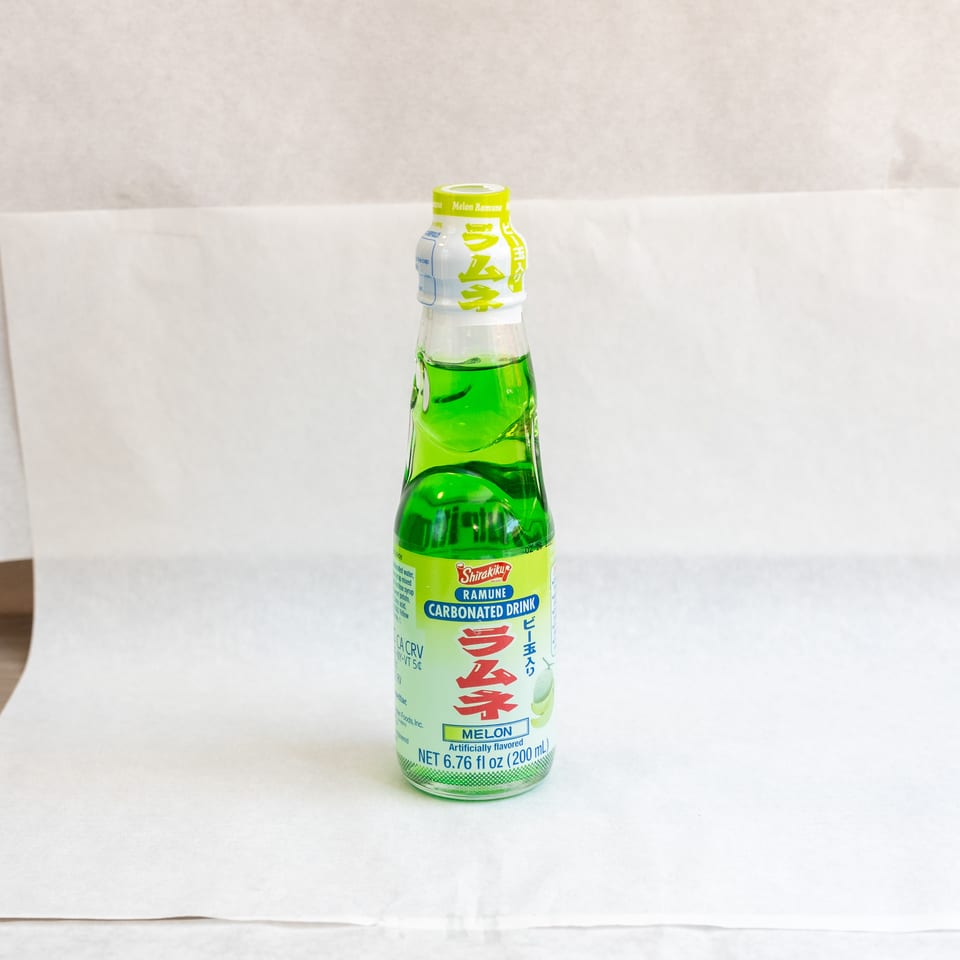 A green bottle of Shirakiku Ramune Melon Carbonated Drink stands on a white surface.