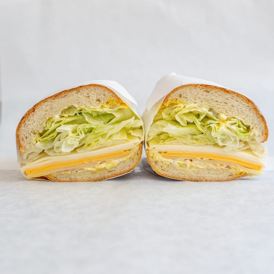 A large sandwich, cut in half, with lettuce, cheese, and mustard on a white background.