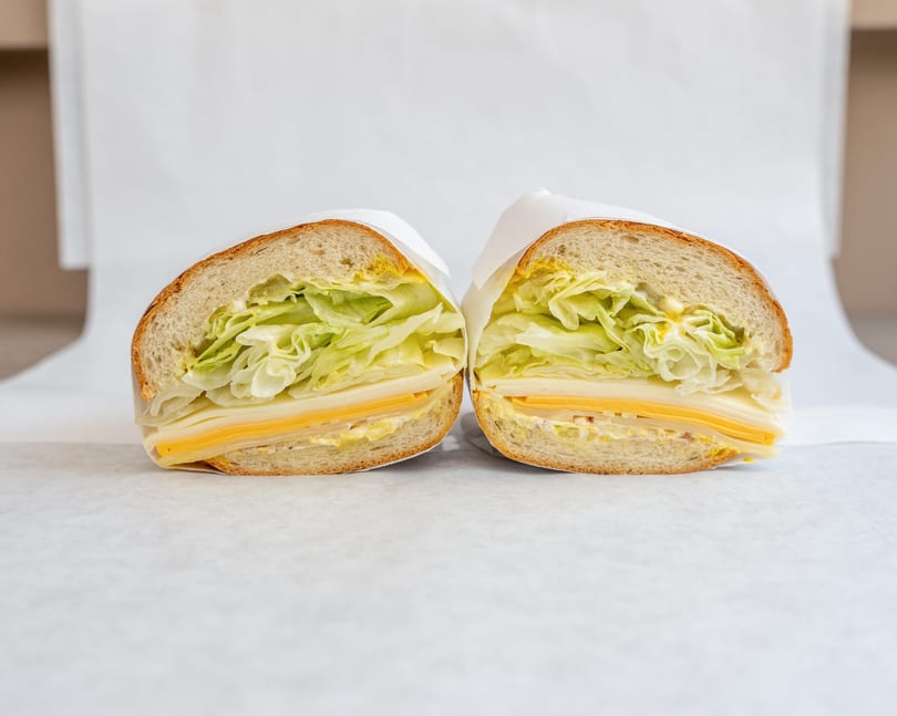 A large sandwich, cut in half, with lettuce, cheese, and mustard on a white background.