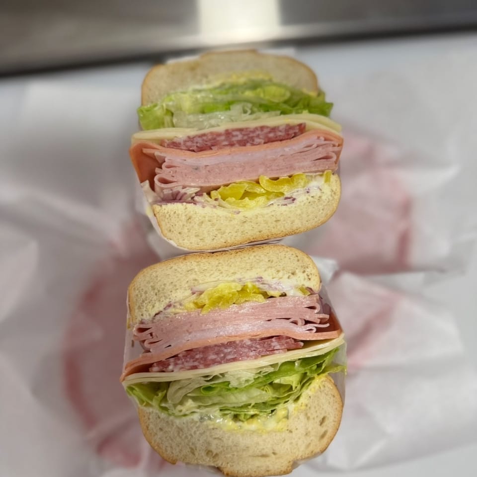 Two halves of a deli sub sandwich with lettuce, cheese, salami, ham, and pickles.
