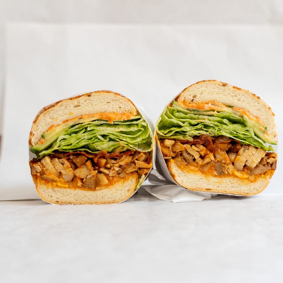 Two halves of a sandwich with chicken, lettuce, and sauce, wrapped in white paper.
