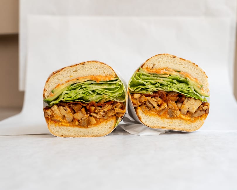 Two halves of a sandwich with chicken, lettuce, and sauce, wrapped in white paper.