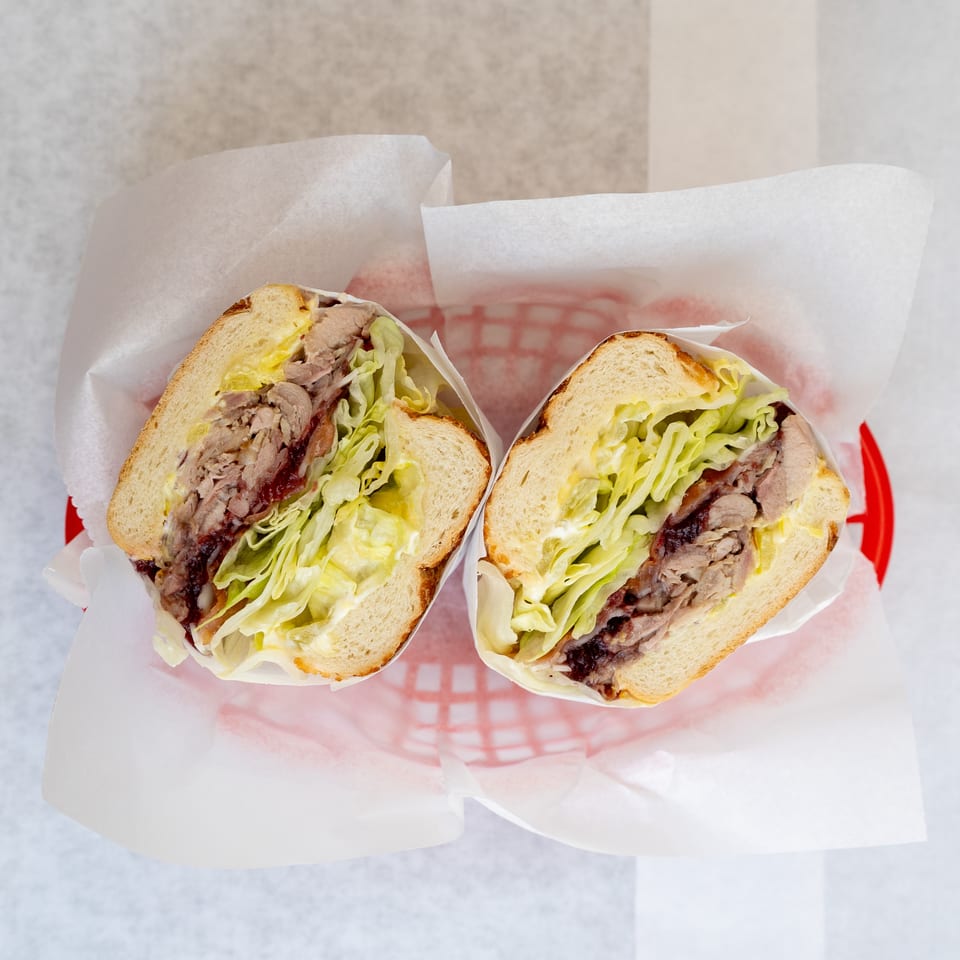 Two halves of a sandwich with meat, lettuce, and sauce, served in a red basket.