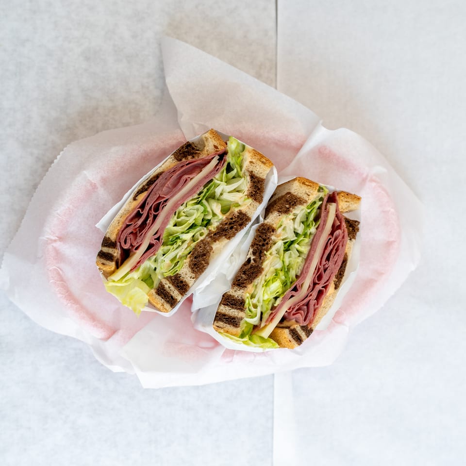 Two deli sandwiches with meat, cheese, and shredded lettuce on marbled rye bread, wrapped in paper.
