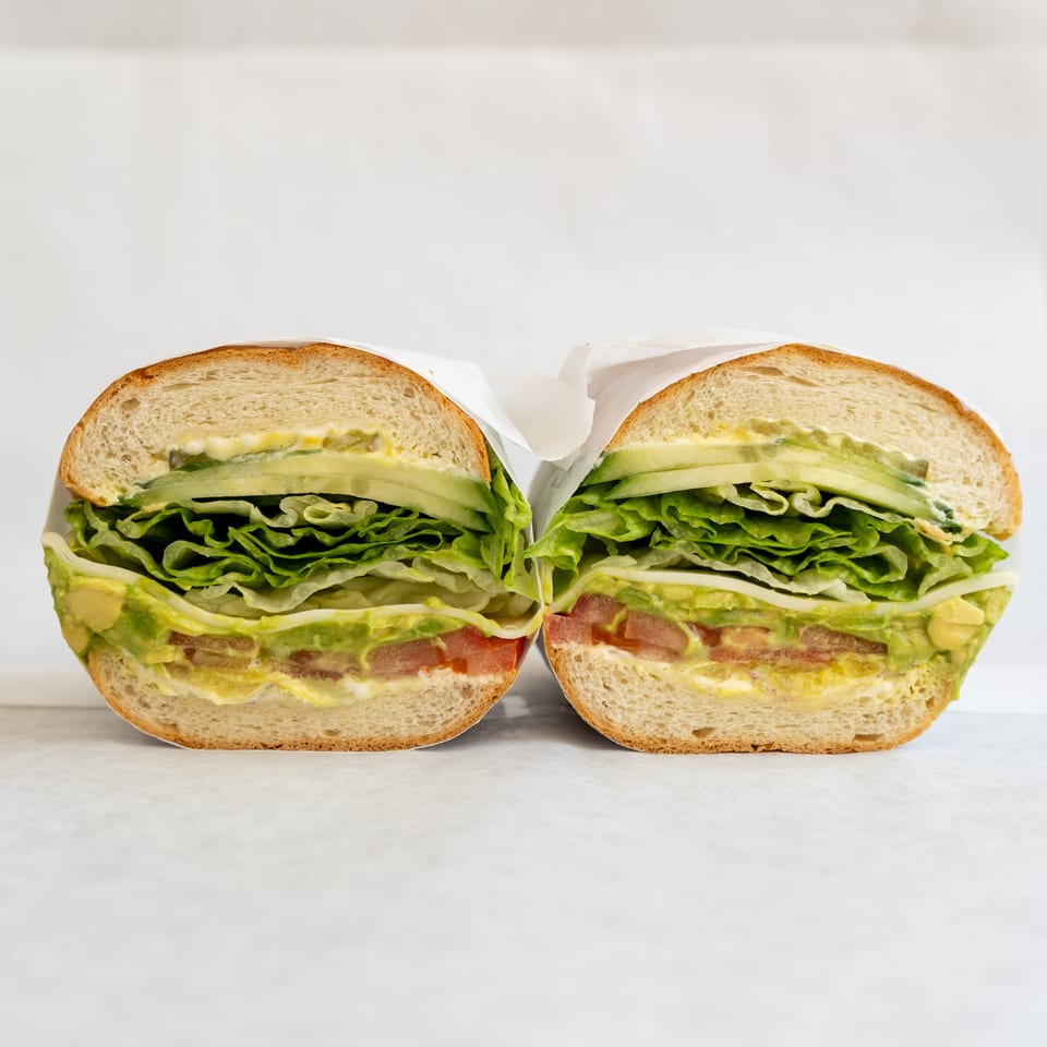 A fresh sandwich, cut in half, revealing layers of lettuce, avocado, tomato, and cucumber.