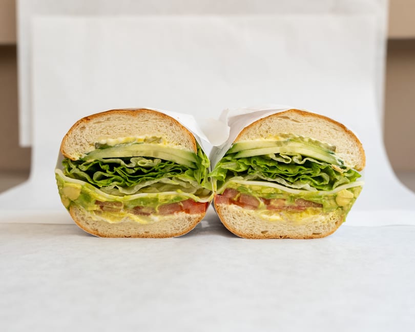A fresh sandwich, cut in half, revealing layers of lettuce, avocado, tomato, and cucumber.