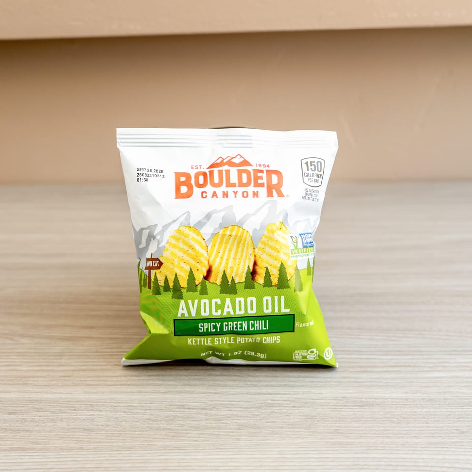 A bag of Boulder Canyon Avocado Oil Spicy Green Chili Kettle Style Potato Chips on a wooden surface.