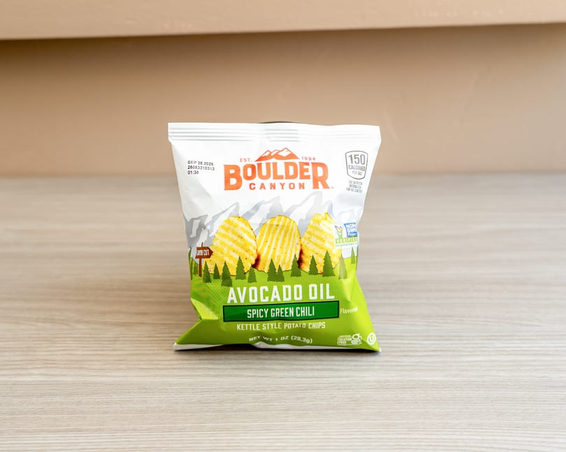 A bag of Boulder Canyon Avocado Oil Spicy Green Chili Kettle Style Potato Chips on a wooden surface.