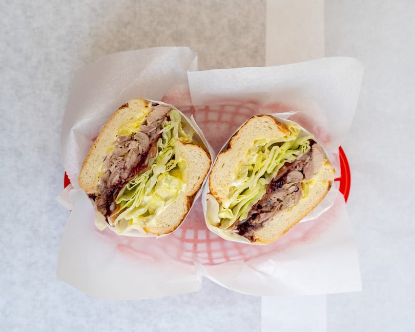 Two halves of a sandwich with meat, lettuce, and sauce, served in a red basket.