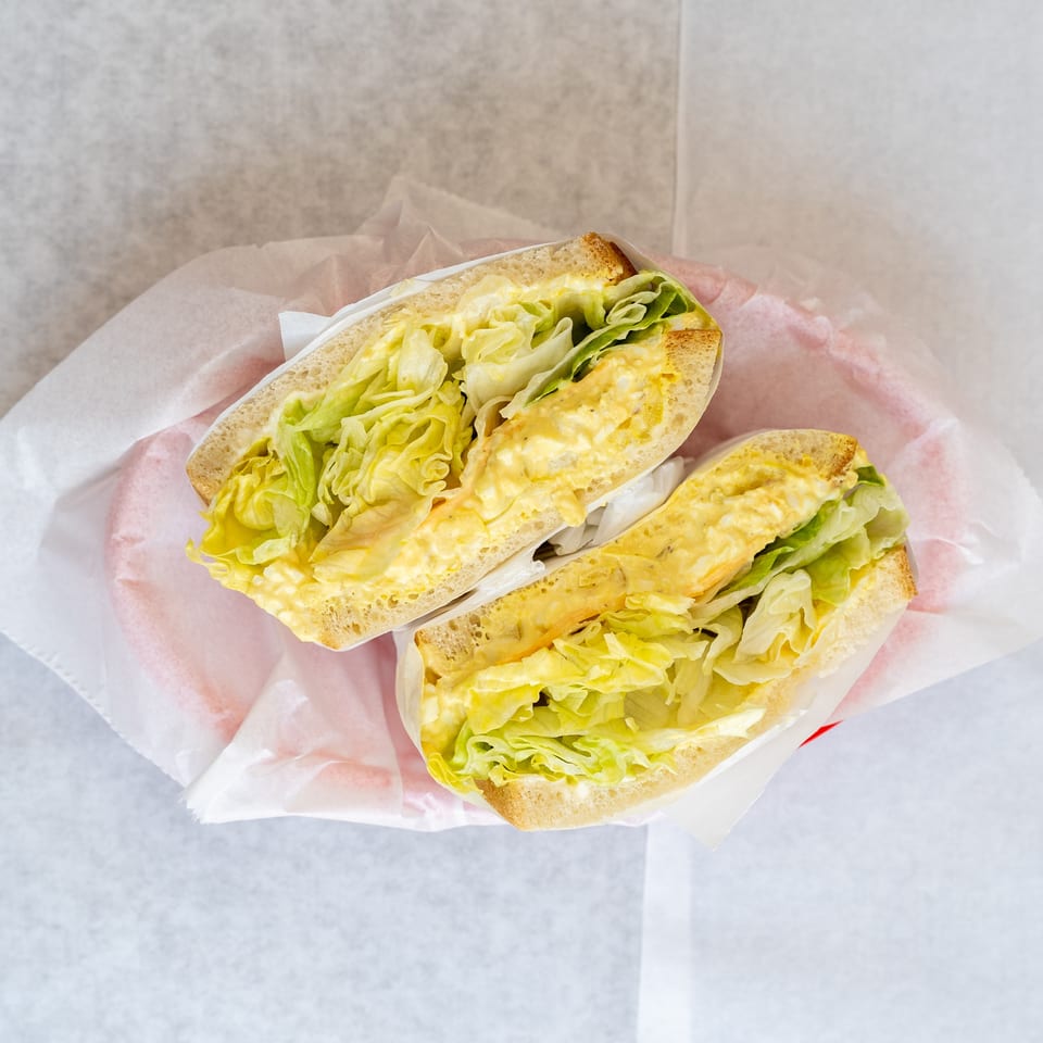 Two halves of an egg salad sandwich with lettuce, served in a red basket lined with white paper.