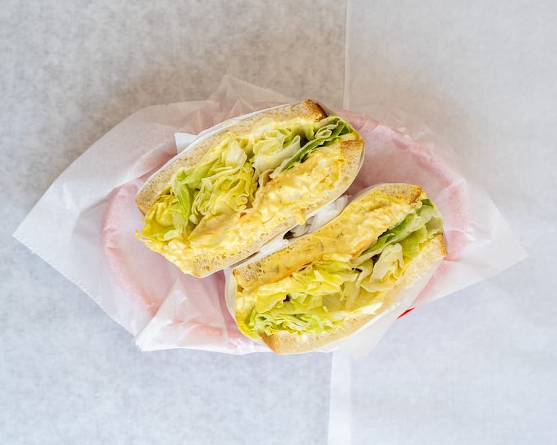 Two halves of an egg salad sandwich with lettuce, served in a red basket lined with white paper.