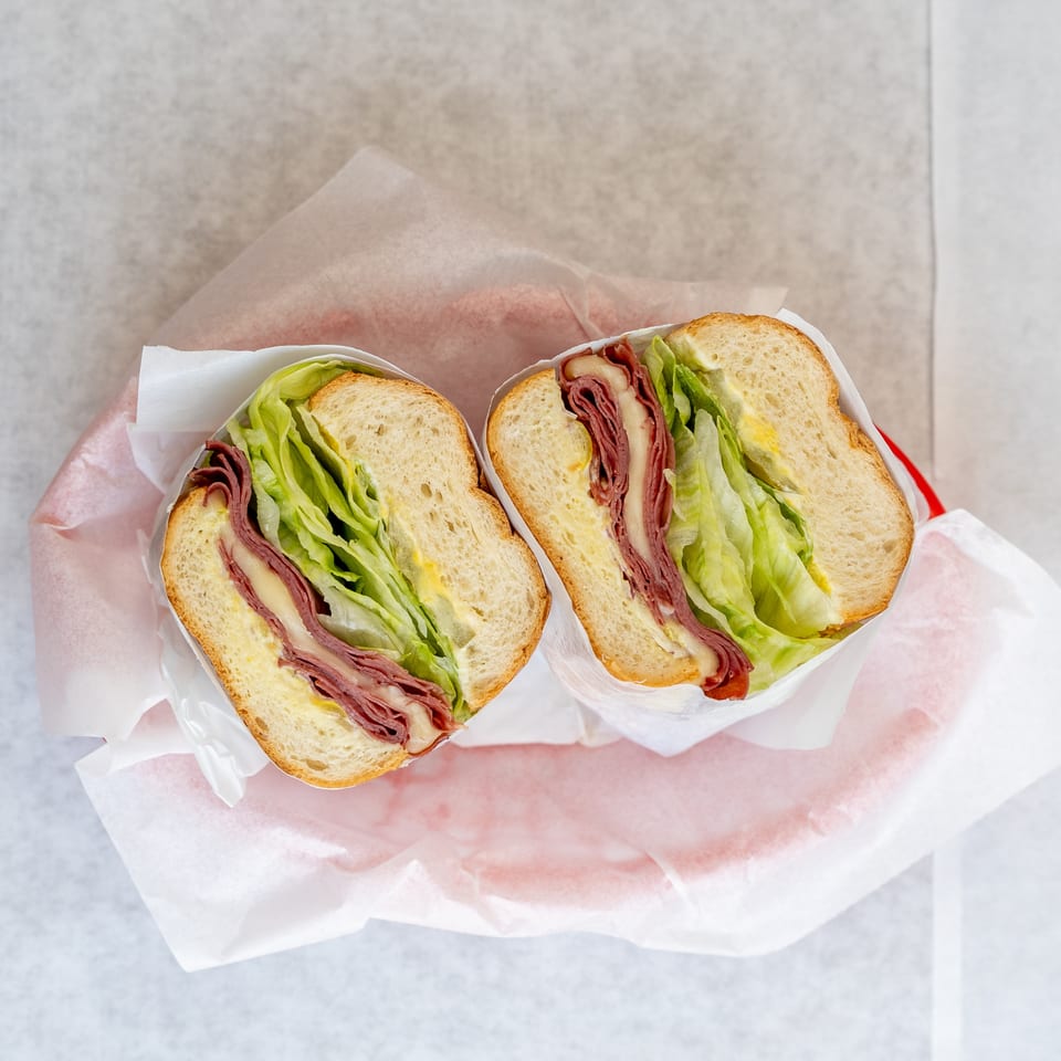 Two halves of a deli sandwich with meat, cheese, lettuce, and mustard, wrapped in paper.