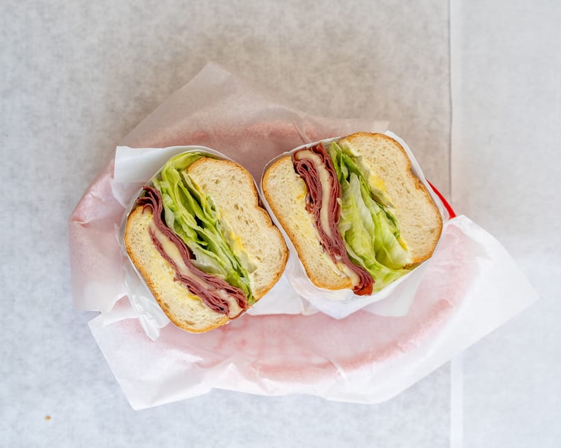 Two halves of a deli sandwich with meat, cheese, lettuce, and mustard, wrapped in paper.