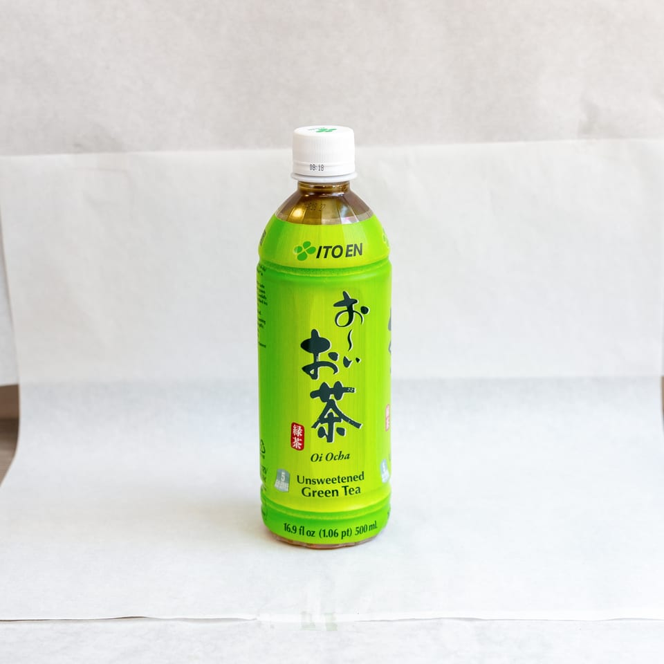 A green bottle of Ito En Oi Ocha Unsweetened Green Tea on a white and wooden surface.