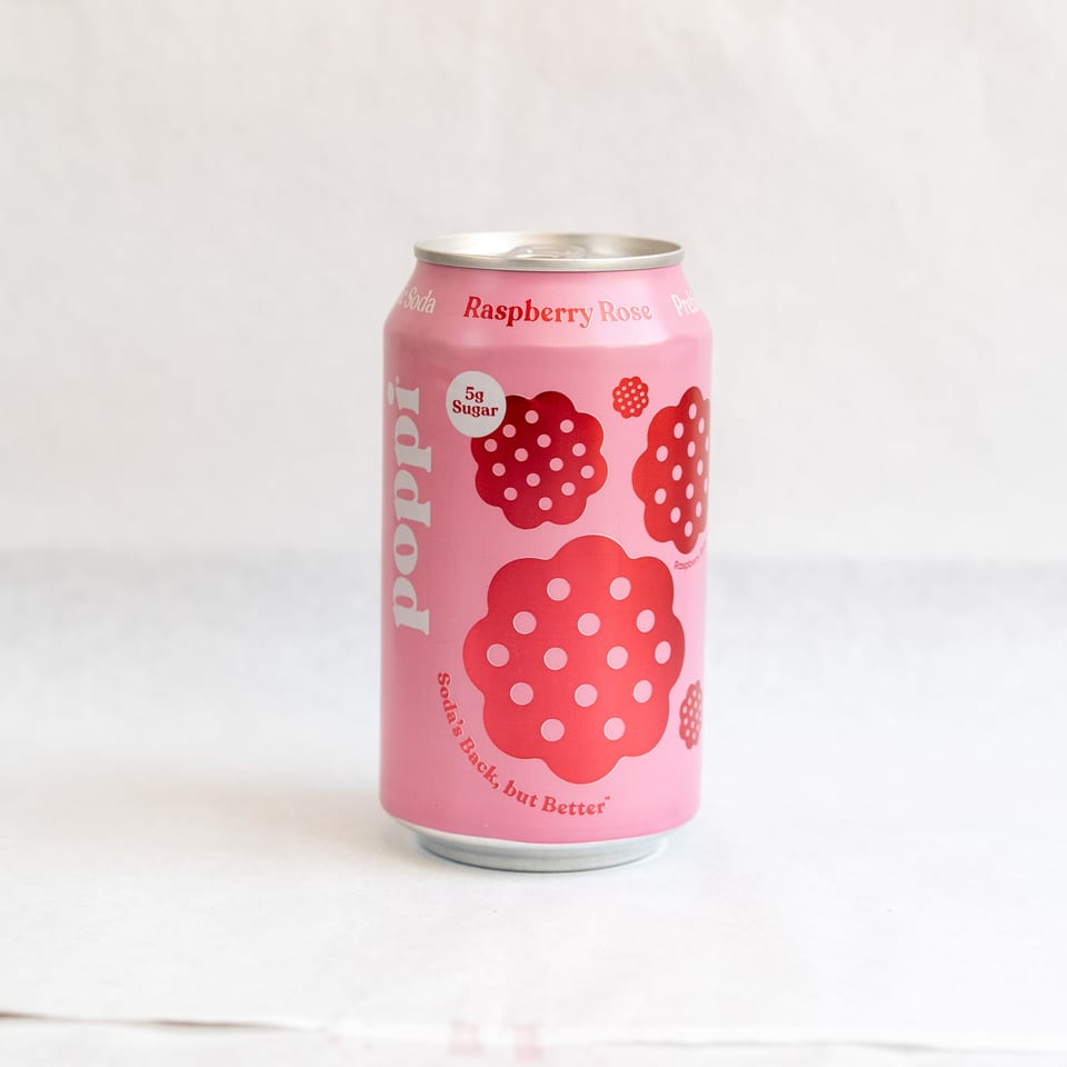A pink Poppi Raspberry Rose soda can with red raspberry designs stands on a white surface.