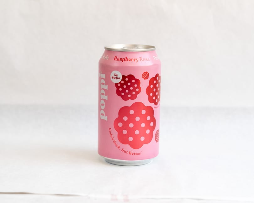 A pink Poppi Raspberry Rose soda can with red raspberry designs stands on a white surface.